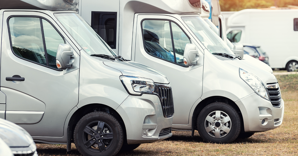 Row of motorhomes parked outdoors showing low-profile bodies and over-cab storage pods, a popular layout for UK touring and resale comparisons.