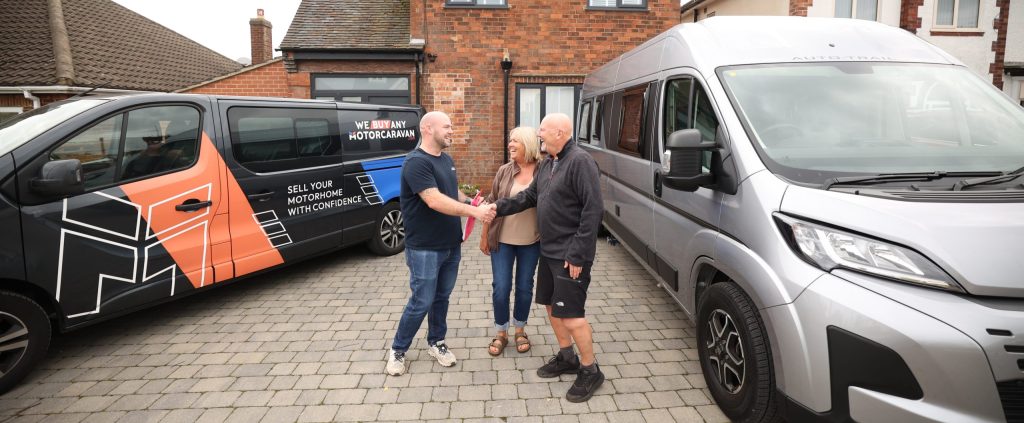 Motorhome owners shaking hands with a We Buy Any Motorcaravan assessor outside a UK home, representing trust, valuations and motorhome selling decisions in 2025.